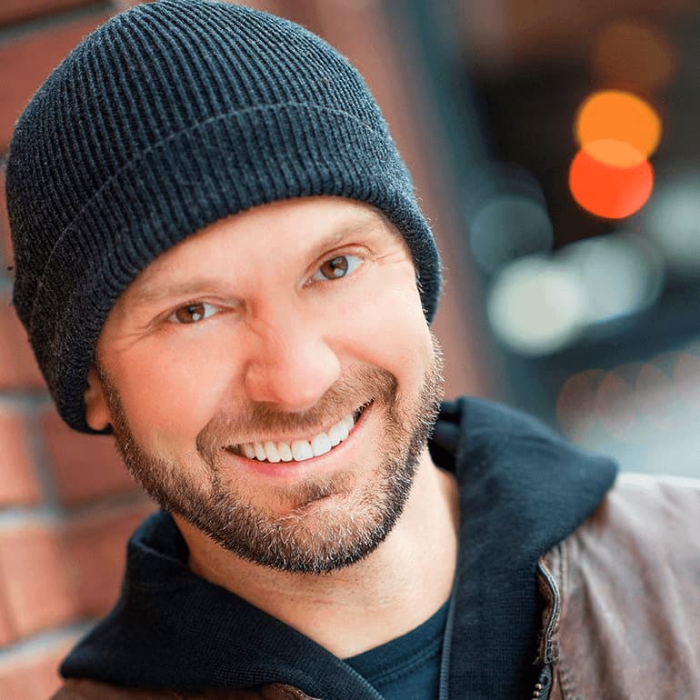 Zack Judson smiling, in a dark knit beanie and hooded jacket, in front of a brick wall.